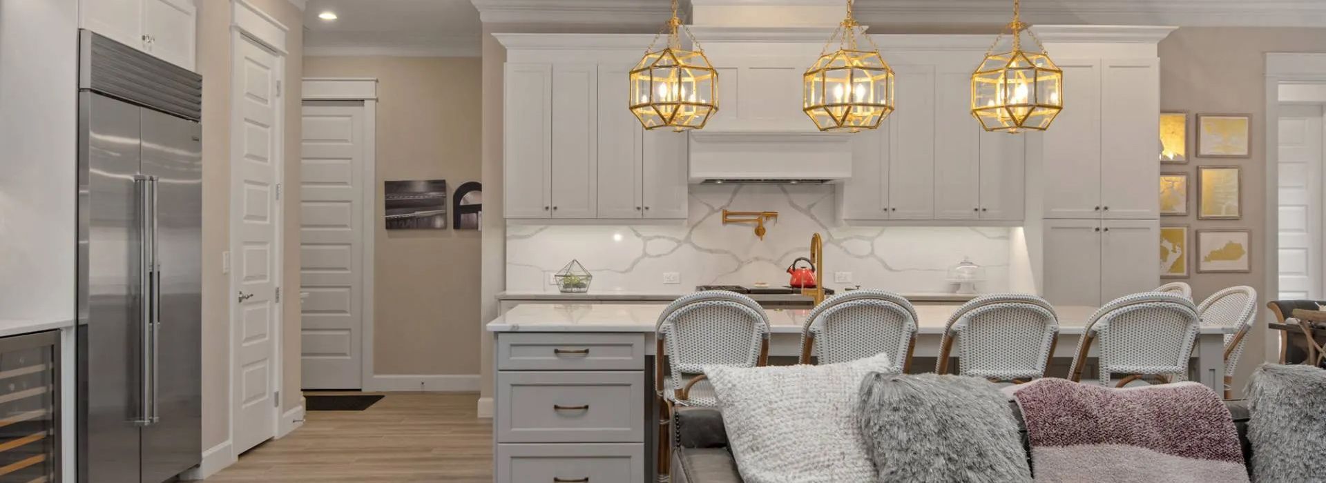 Bright kitchen with marble island, gold pendant lights, white cabinets, and upholstered stools attached to a dining area