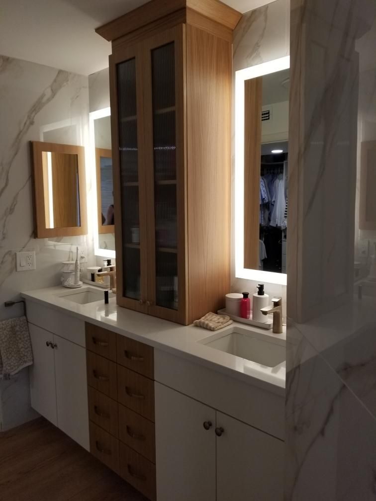 Bathroom vanity with wood cabinets, white countertop, mirror, and lit sconces beside a shower curtain.