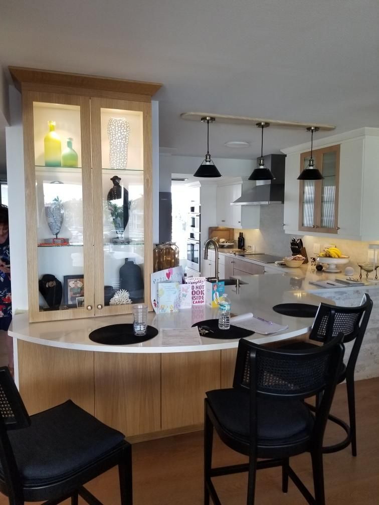 Modern kitchen with island, black chairs, pendant lights, and a glass-front cabinet with decor