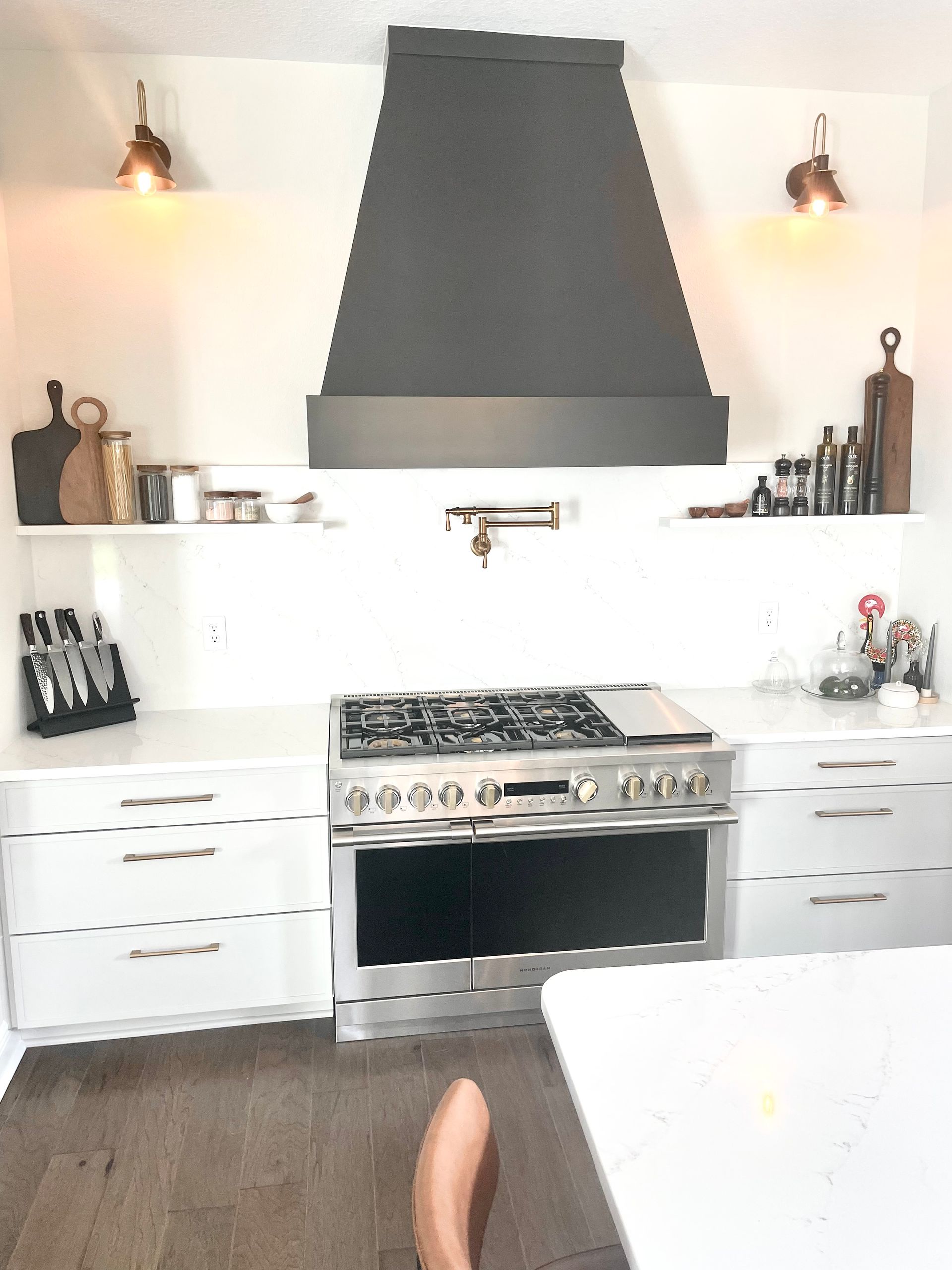 Bright white kitchen with black range hood, stainless stove, and wooden floor; dining table in foreground