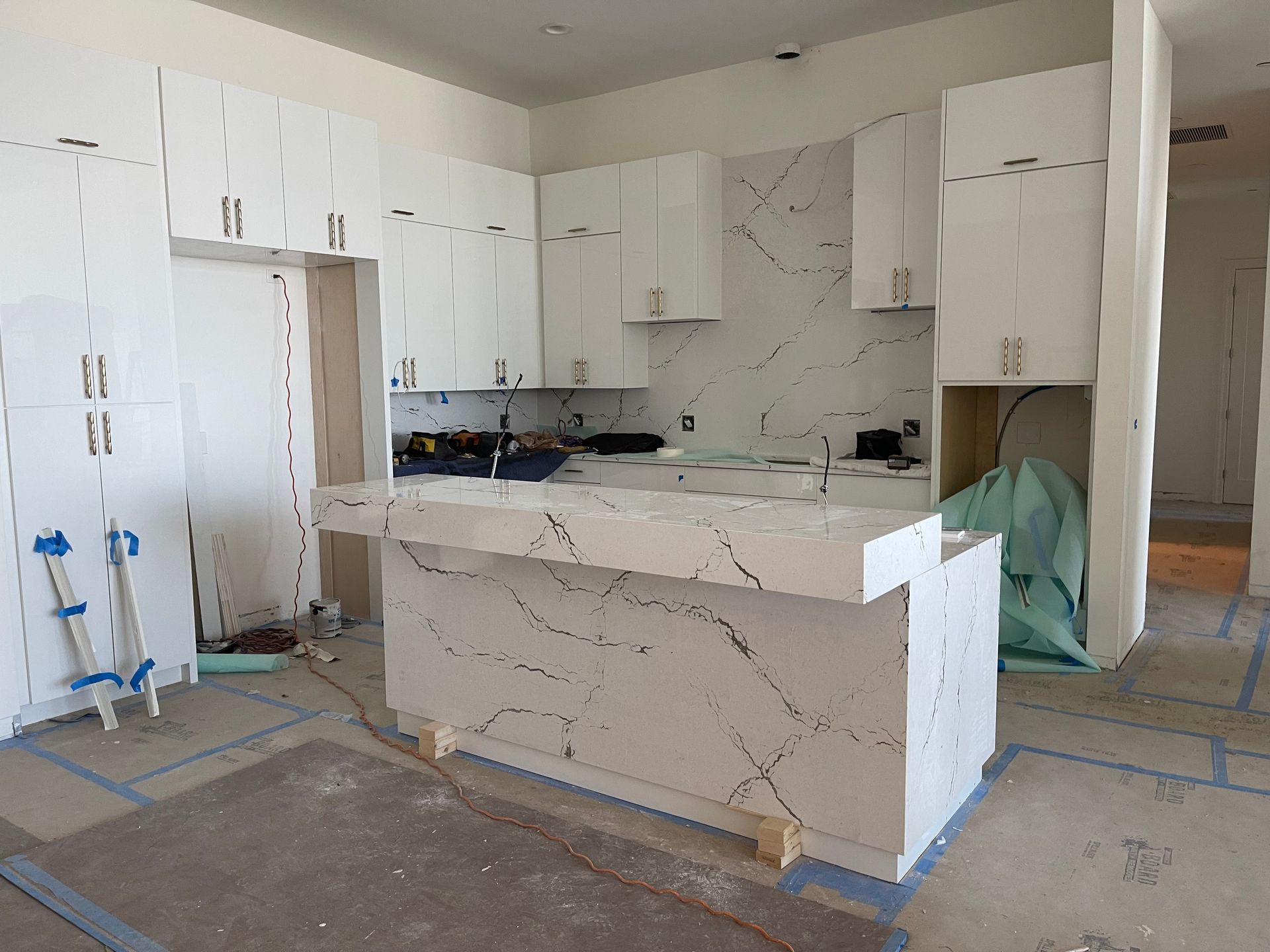 Under-construction kitchen with white cabinets, marble-look island, and tools on the floor
