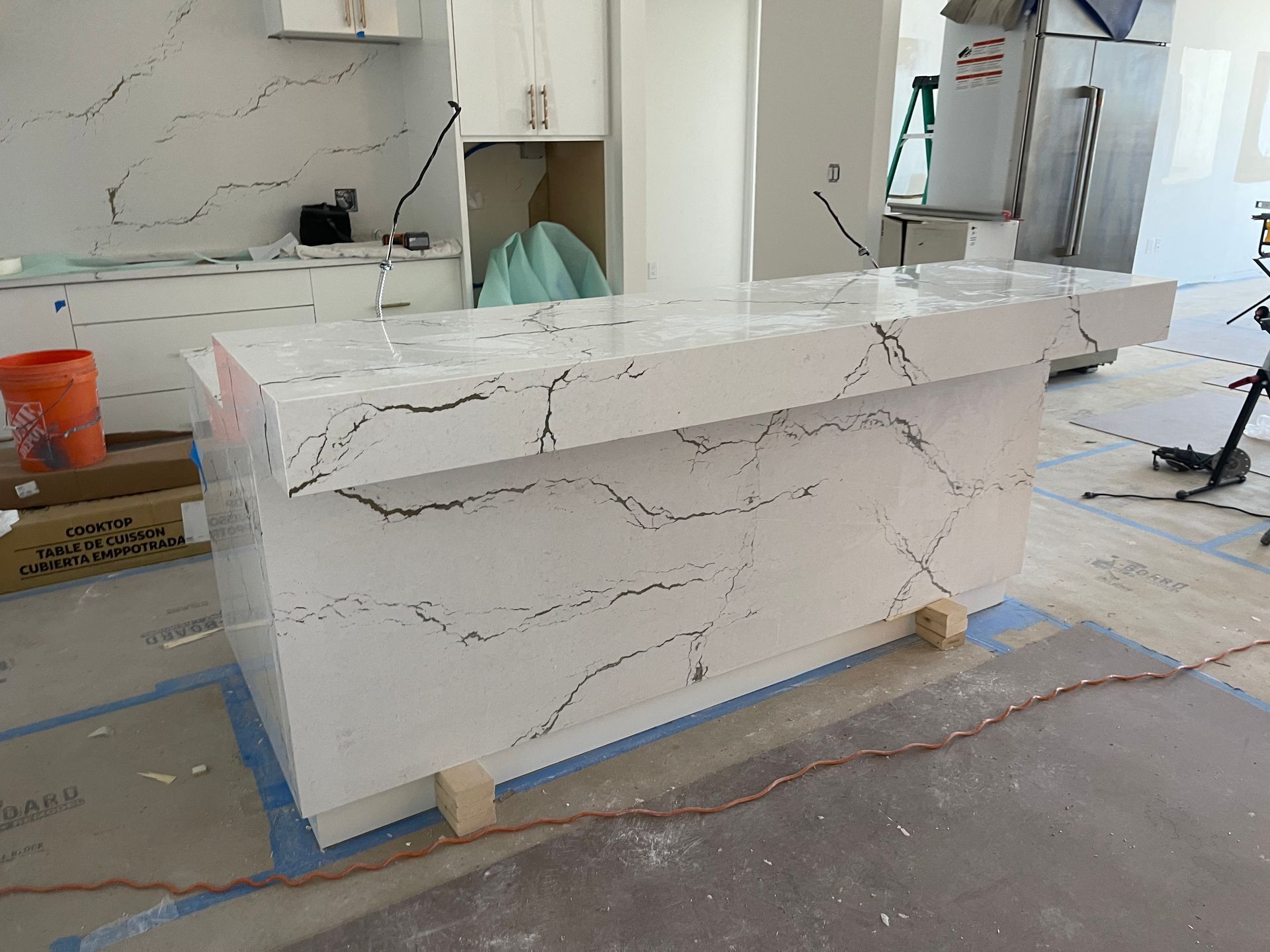 White marble-look kitchen island cabinet on a workshop floor, partially wrapped and awaiting installation