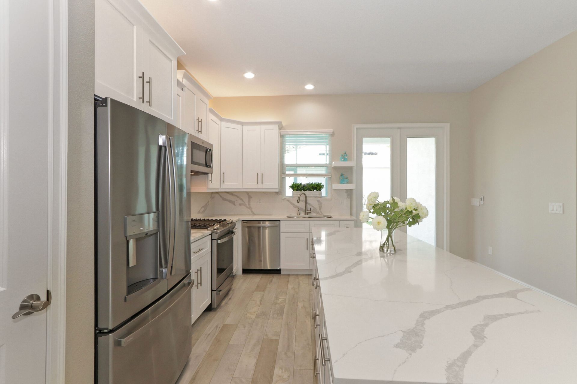 Bright modern kitchen with white cabinets, stainless steel appliances, and a long marble island