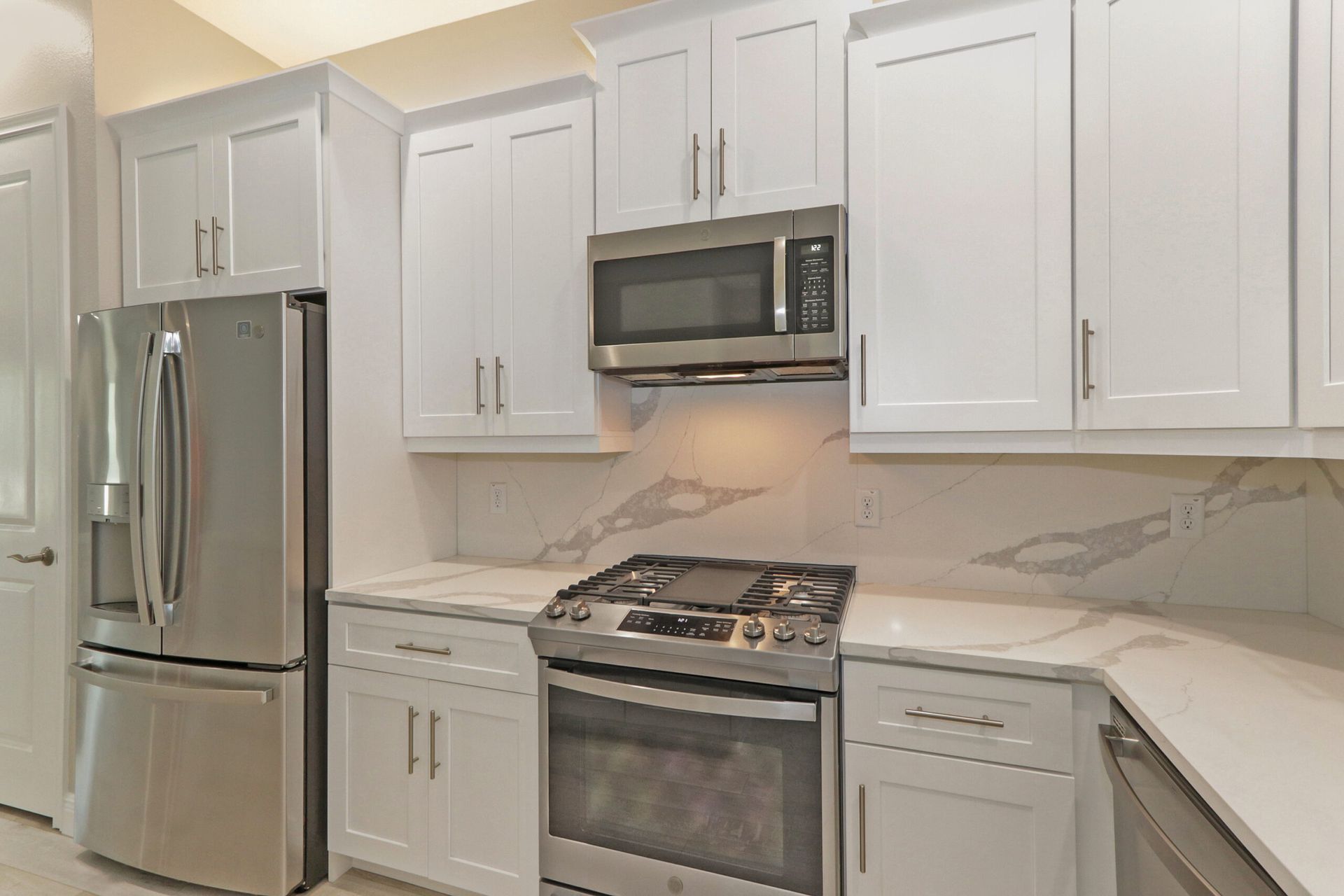 Modern white kitchen with stainless steel appliances, gray cabinets, and a gas stove with microwave above