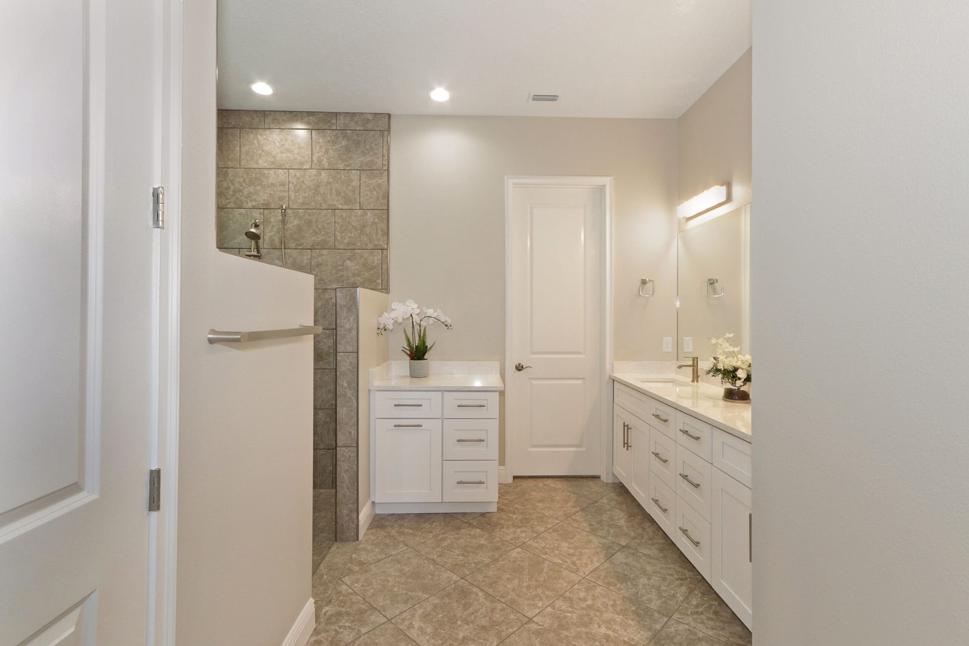 Bright bathroom with double vanity, white cabinets, stone shower, and beige tile floor.