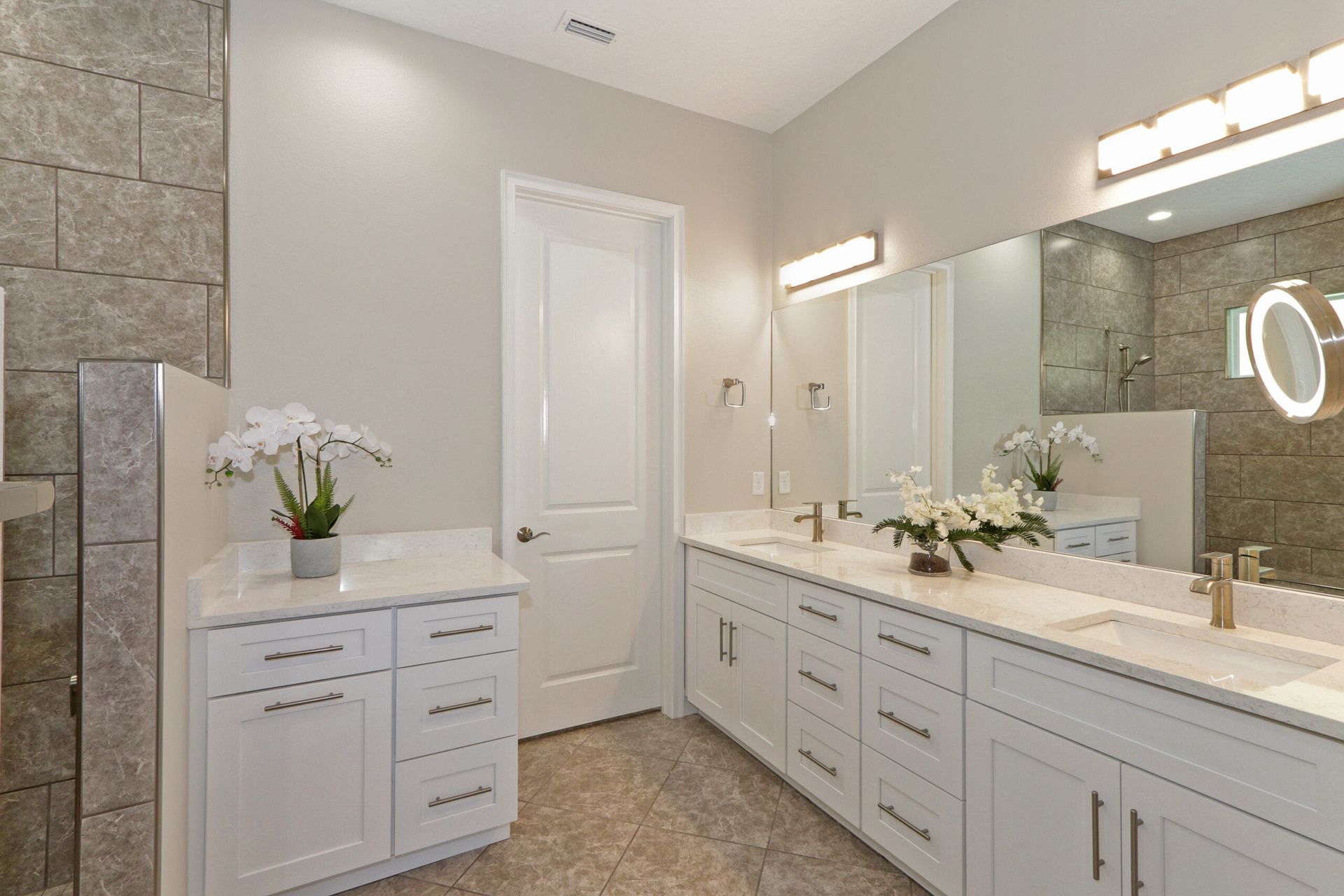 Modern bathroom with double vanity, large mirror, white cabinetry, and stone tile walls and floor