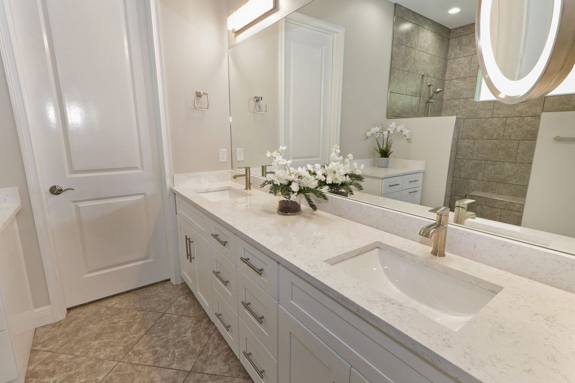 Bright modern bathroom with long white vanity, double sinks, marble countertops, and large mirror