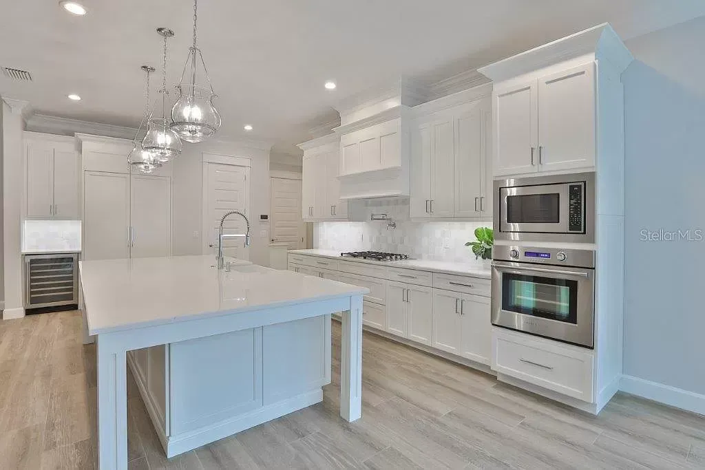 Bright white modern kitchen with island, pendant lights, stainless appliances, and light wood floors