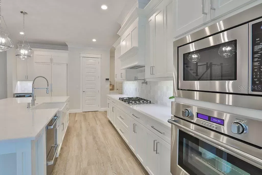 Bright white modern kitchen with island, stainless steel appliances, and wood floor