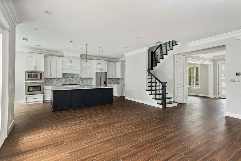 Spacious open-plan kitchen and living area with dark wood floors, white cabinets, and staircase