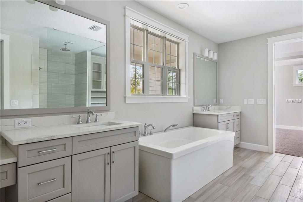 Bright white bathroom with double vanity, large mirror, window, bathtub, and walk-in shower