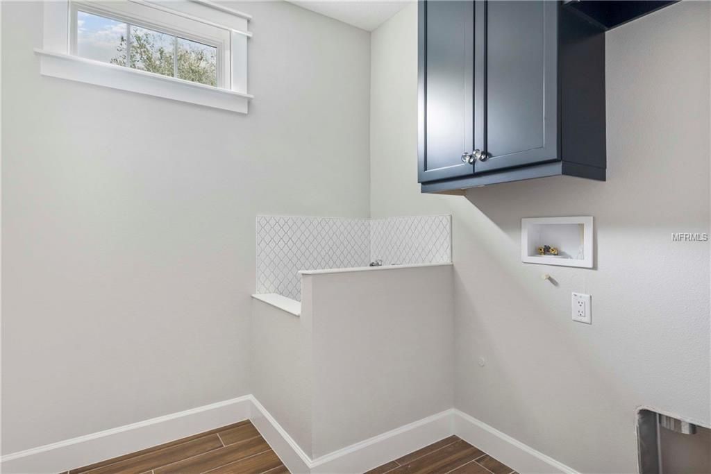 Laundry room with white walls, dark cabinets, small window, and patterned tile backsplash.