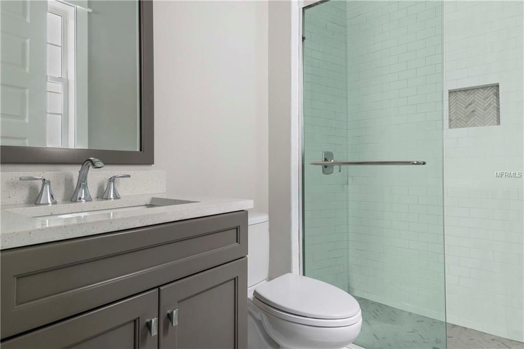 Modern bathroom with gray vanity, mirror, toilet, and frosted glass shower door