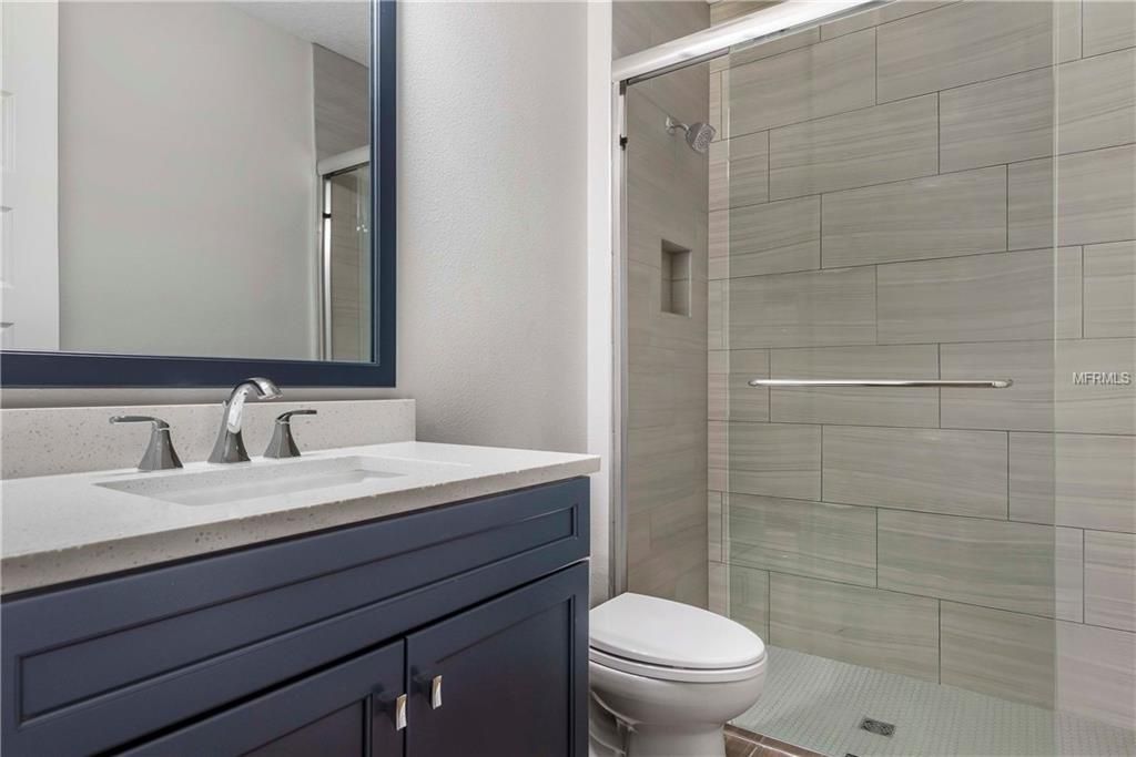 Modern bathroom with navy vanity, white sink, mirror, toilet, and glass-enclosed shower.