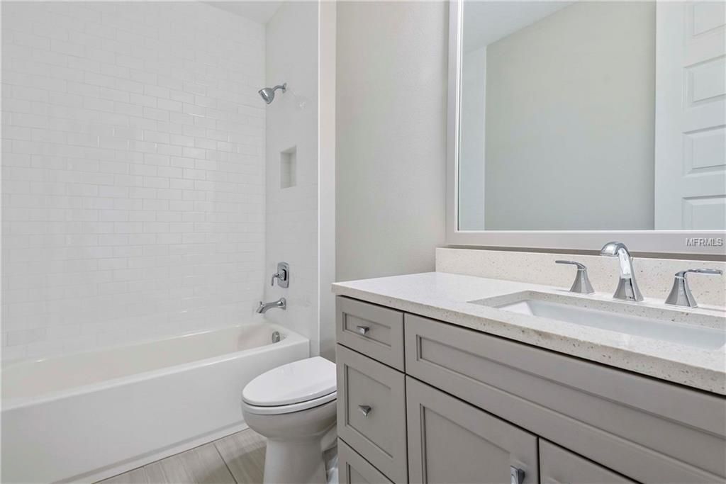 Bright bathroom with a white tub, toilet, and gray vanity with sink and mirror.