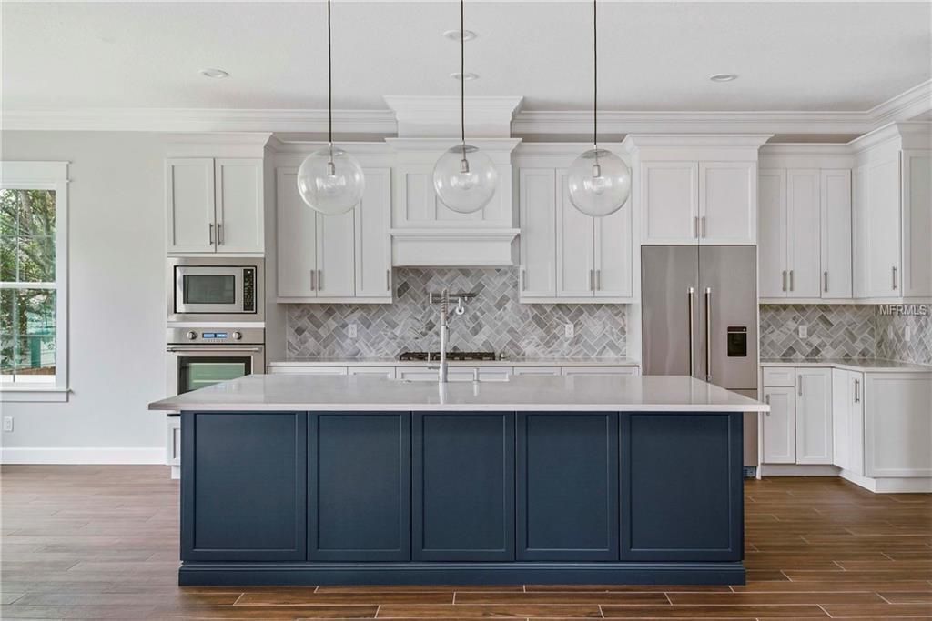Bright modern kitchen with navy island, white cabinets, marble countertops, and pendant lights
