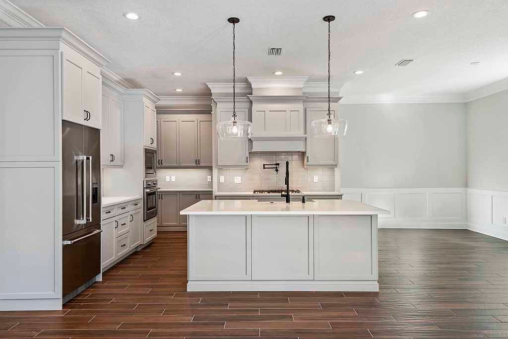 Bright modern kitchen with white cabinets, island, stainless fridge, pendant lights, and dark wood floors