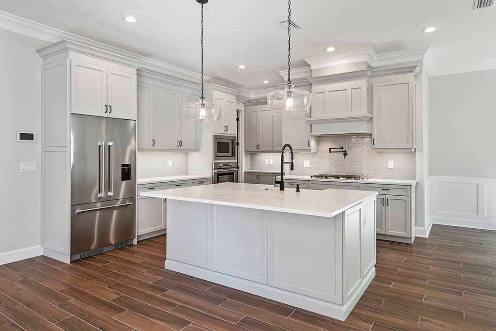 Bright modern white kitchen with stainless steel refrigerator, large island, and pendant lights