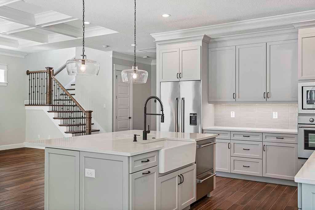 Bright modern kitchen with white cabinets, island, stainless appliances, and staircase in the background