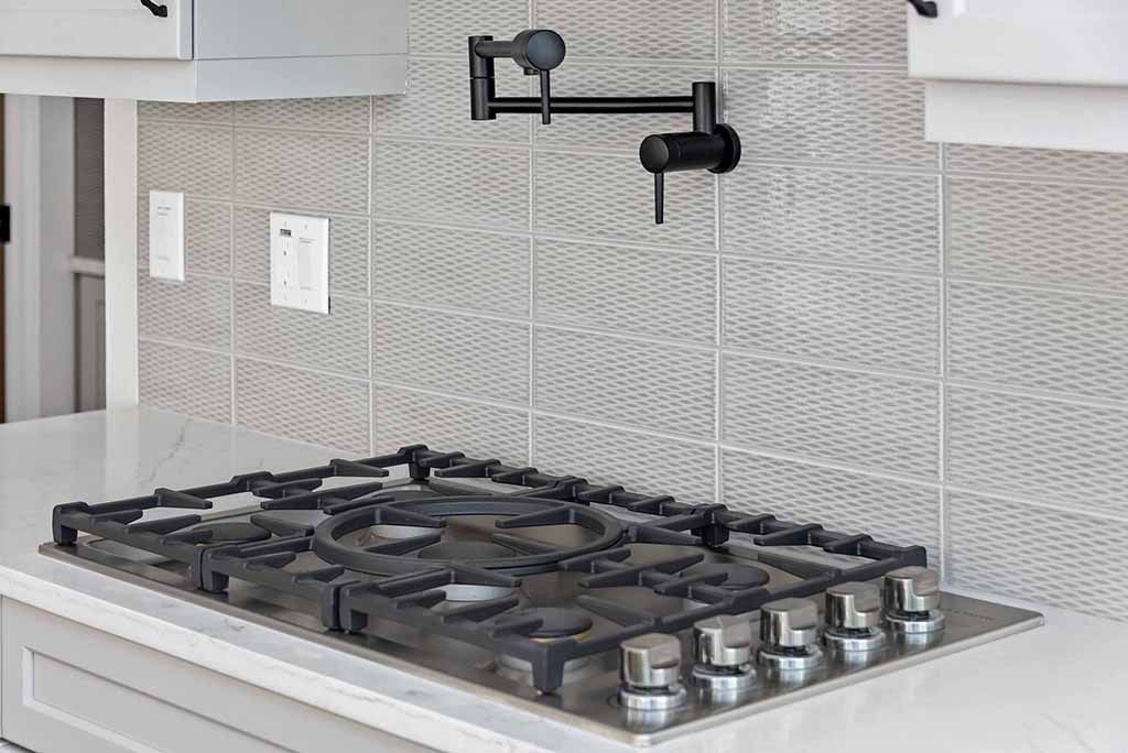 Modern kitchen with stainless steel gas cooktop, tiled backsplash, and wall-mounted pot filler faucet