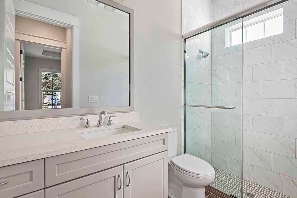 Bright modern bathroom with white vanity, large mirror, and glass-enclosed shower.