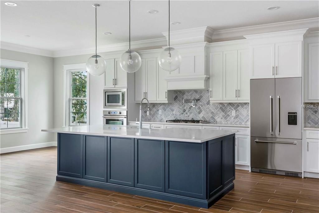 Bright kitchen with navy island, white cabinets, stainless appliances, and large windows