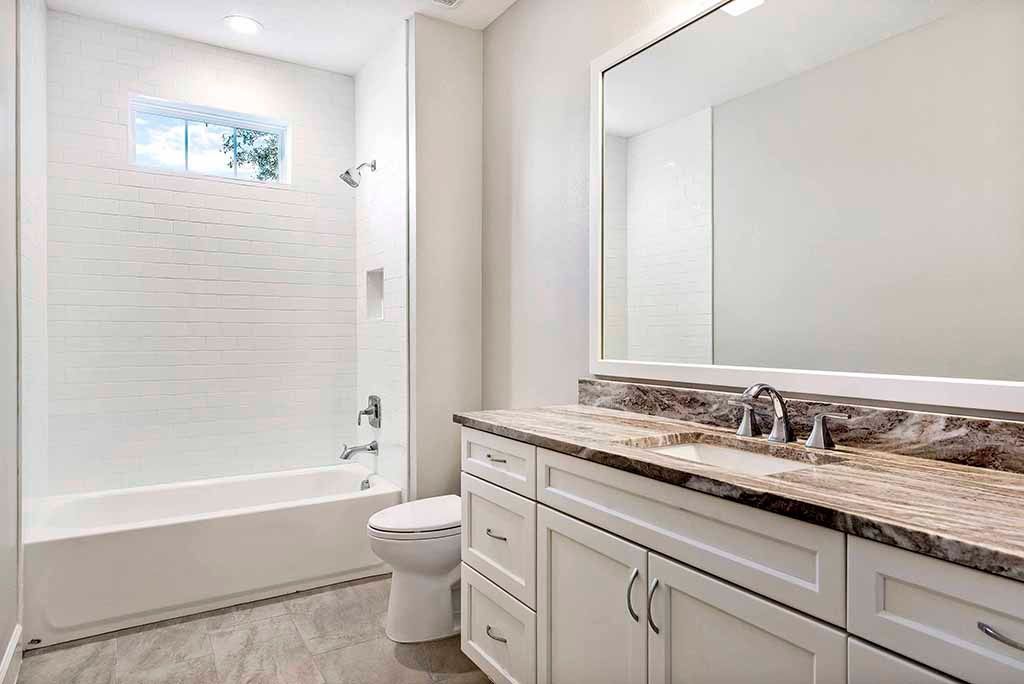 Bright bathroom with bathtub, toilet, and white vanity with large mirror.