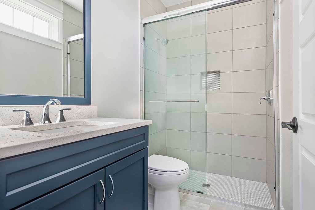 Bathroom with blue vanity, white countertop, mirror, toilet, and glass shower enclosure