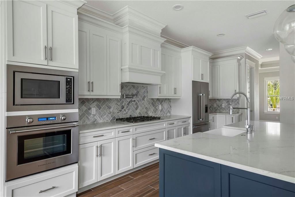 Bright white modern kitchen with stainless appliances, blue island, and marble countertops