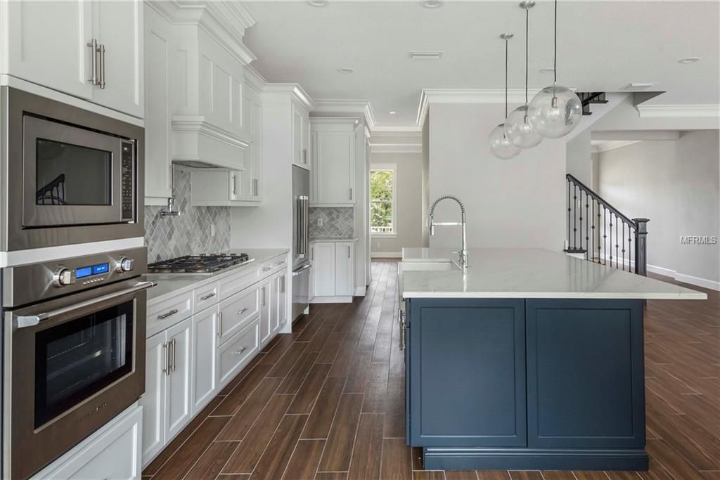 Bright white kitchen with dark wood floors, stainless appliances, and a blue island.