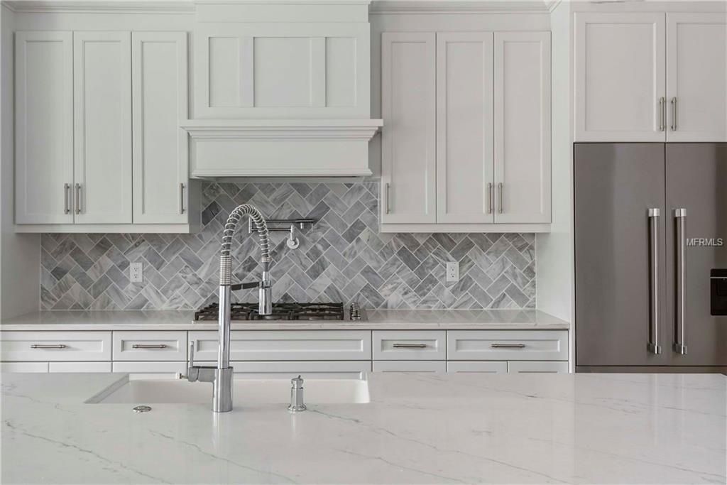 Modern white kitchen with marble island, silver faucet, and stainless steel refrigerator