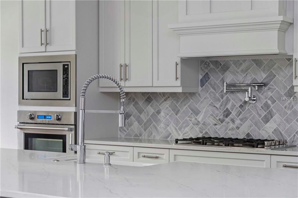 Modern white kitchen with stainless steel appliances, marble island, and herringbone backsplash