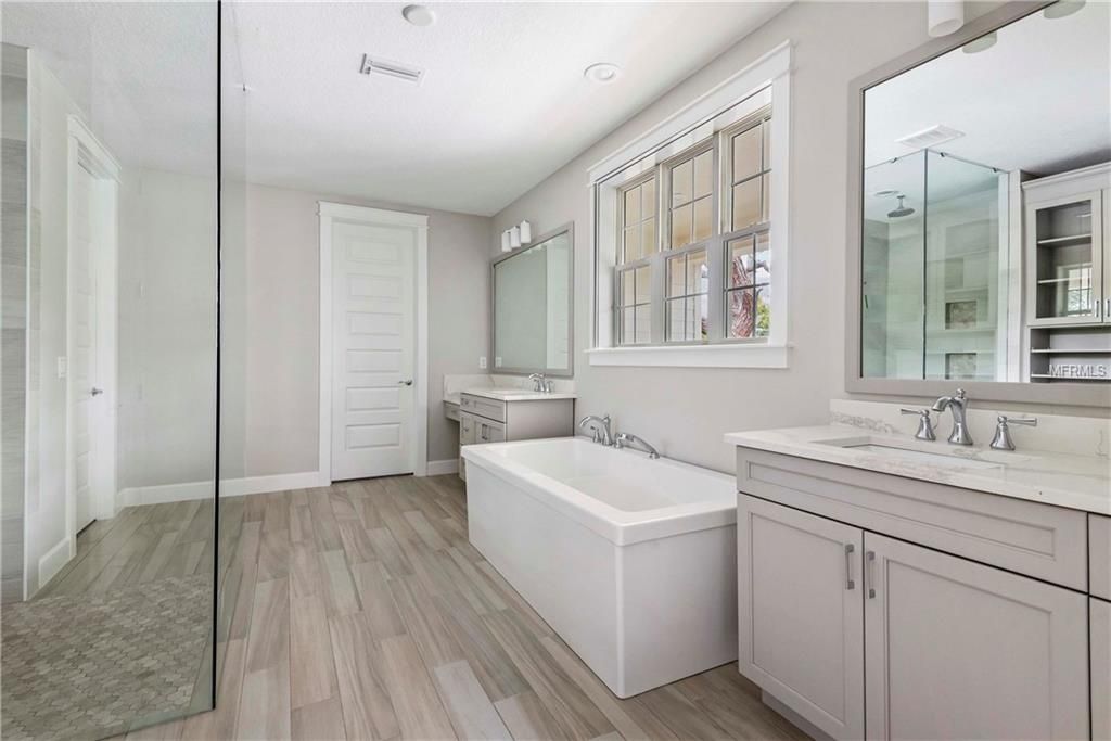Bright modern bathroom with glass shower, freestanding tub, and vanity in white and gray tones