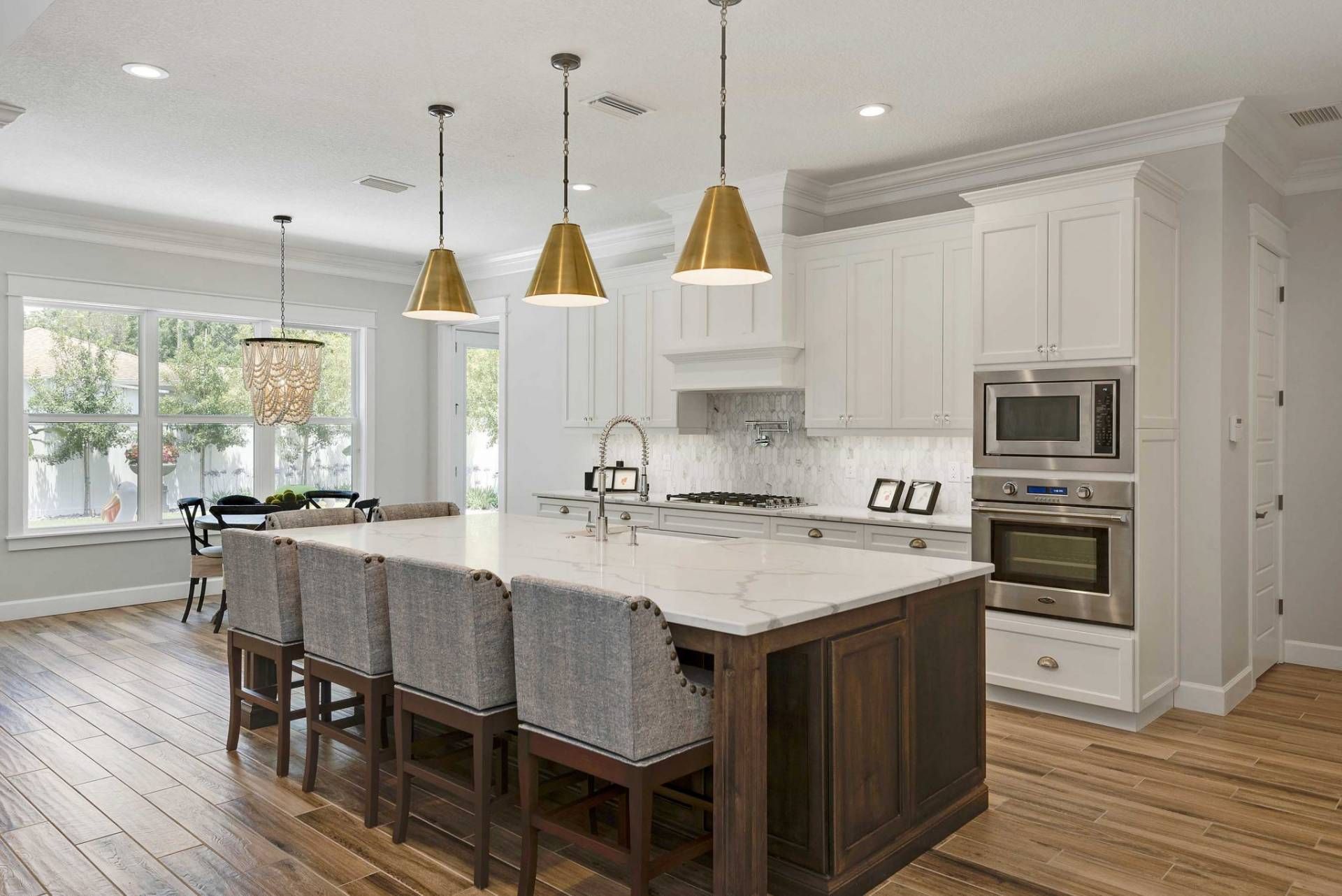 Modern white kitchen with island, pendant lights, marble countertops, and wood floors