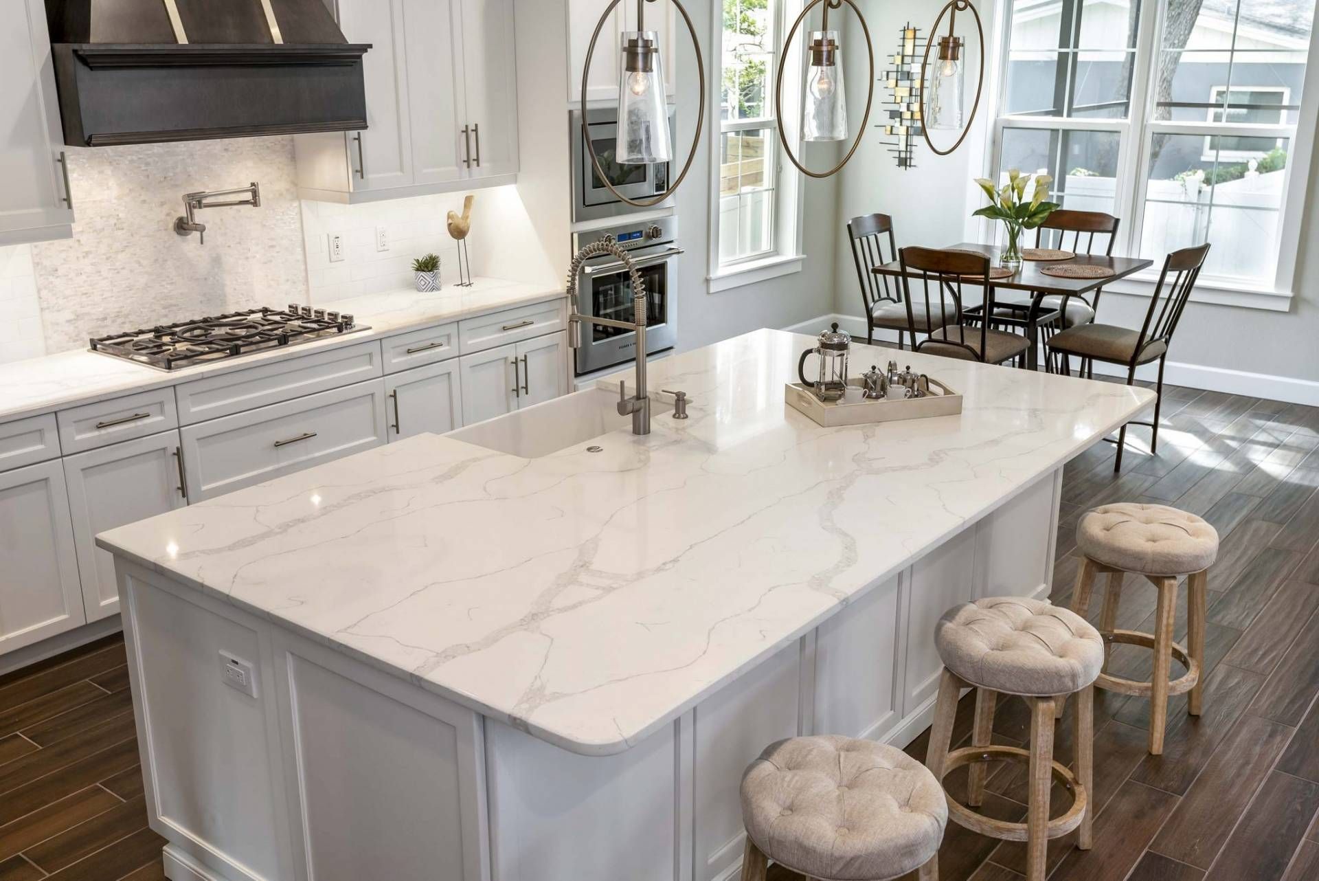 Bright white kitchen with a large marble island, bar stools, and a dining area by tall windows.