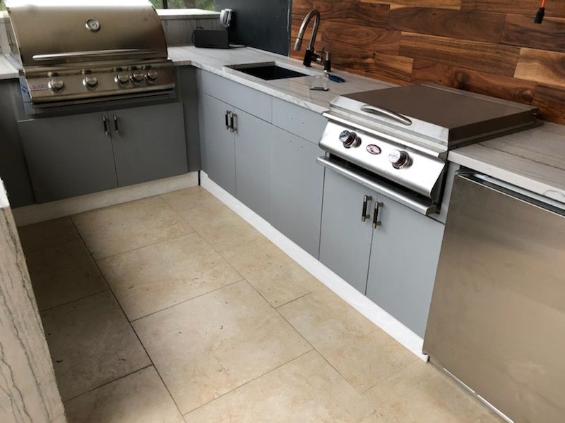 Modern outdoor kitchen with grill, sink, gray cabinets, stainless appliances, and beige tile floor