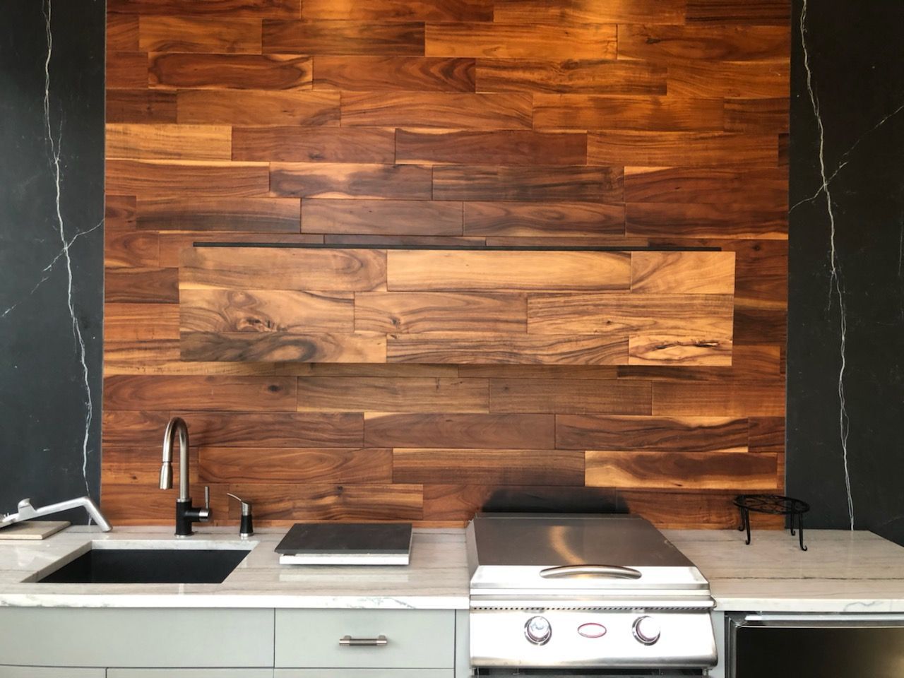 Modern kitchen with wood backsplash, black-and-white countertops, sink, and stainless steel stove