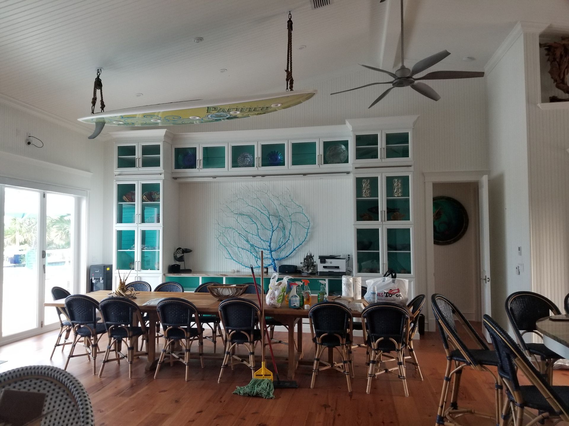 Spacious dining room with long table, many chairs, surfboard decor, and a large ceiling fan.