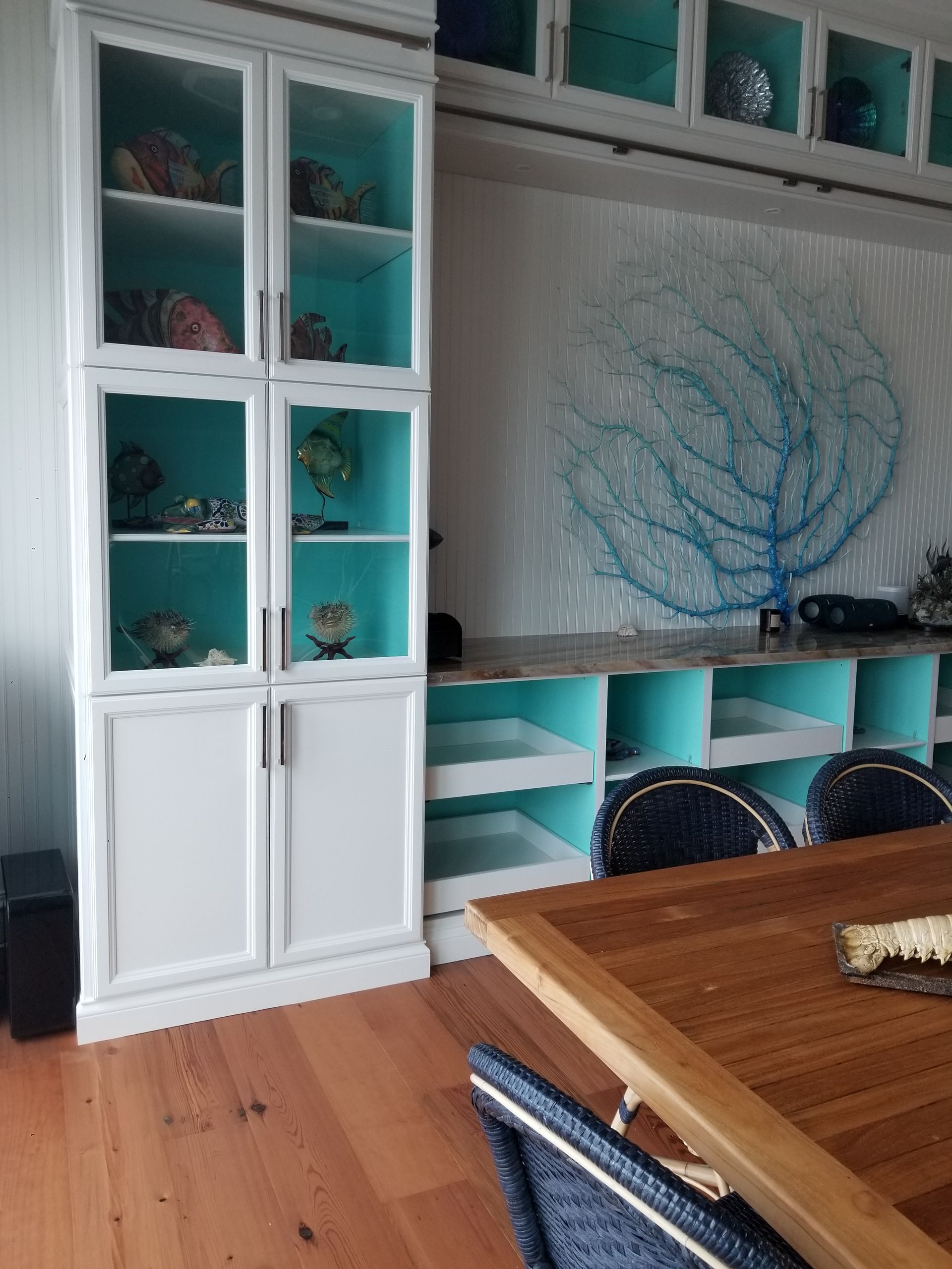 Turquoise and white built-in shelving beside a wooden dining table in a bright room