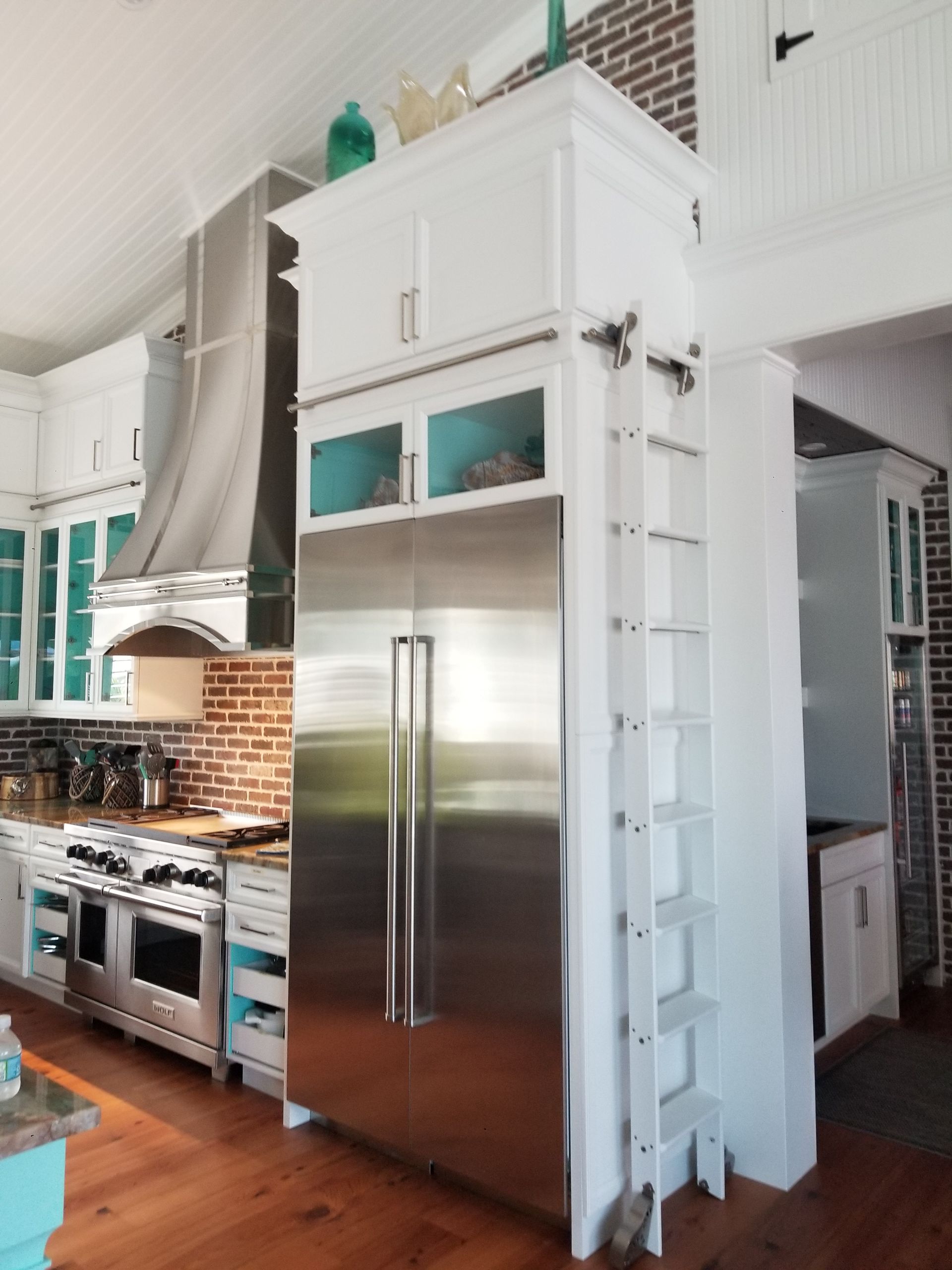 White kitchen with stainless steel refrigerator and oven beside a large range hood and turquoise cabinets