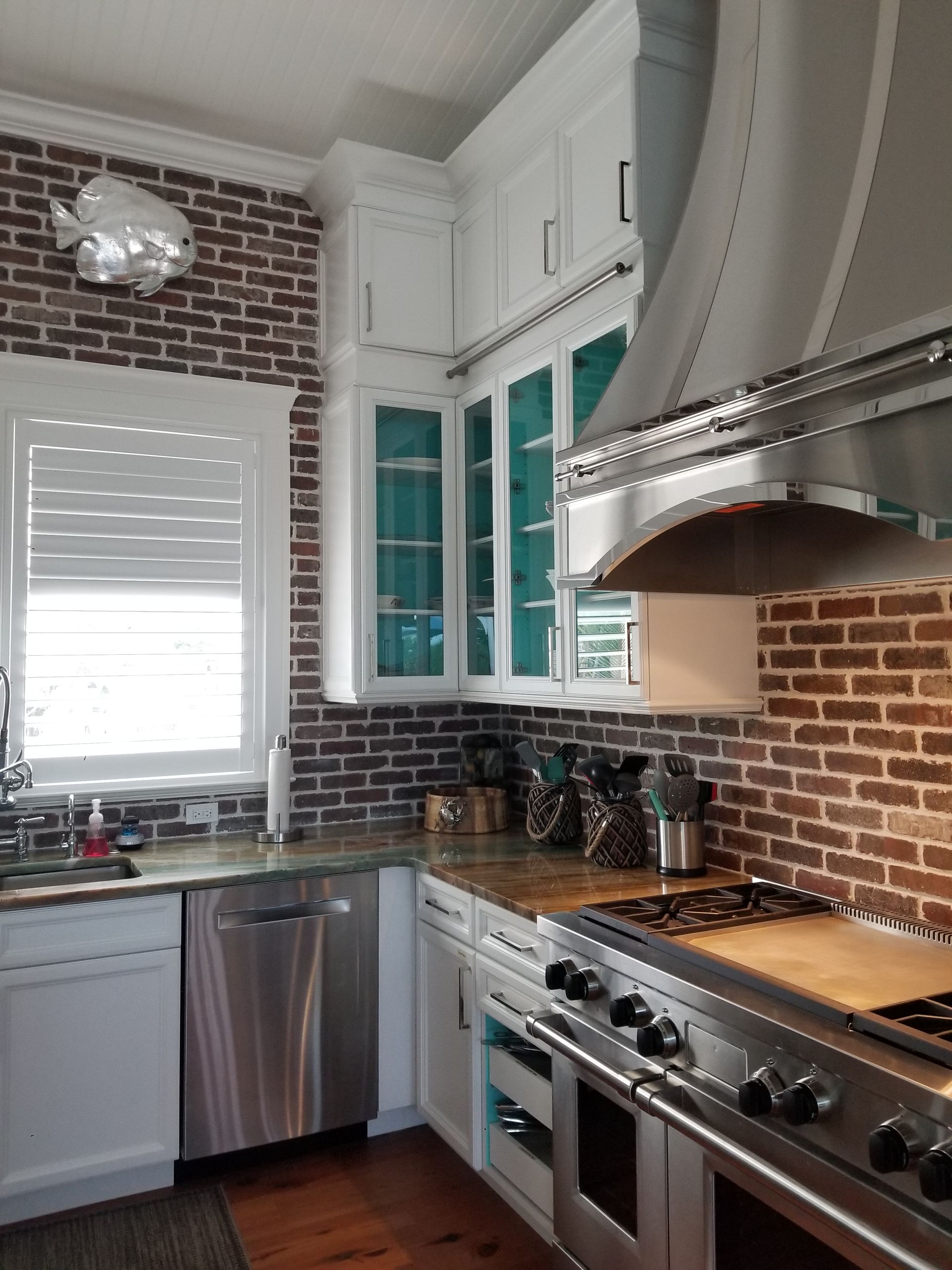 Bright kitchen with brick backsplash, white cabinets, stainless steel appliances, and a window over the sink