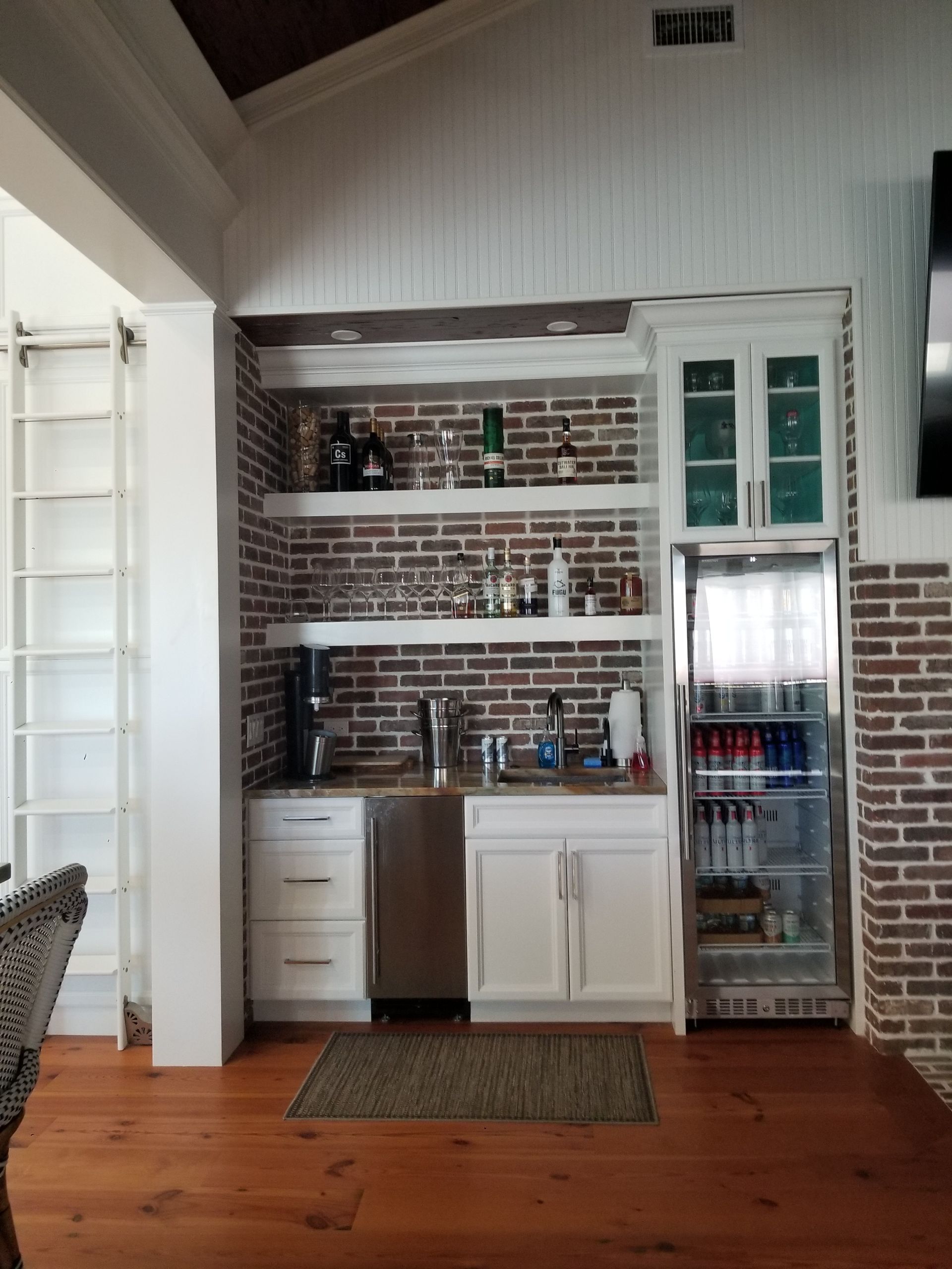 Kitchen nook with brick backsplash, white cabinets, sink, and a glass-front beverage fridge.