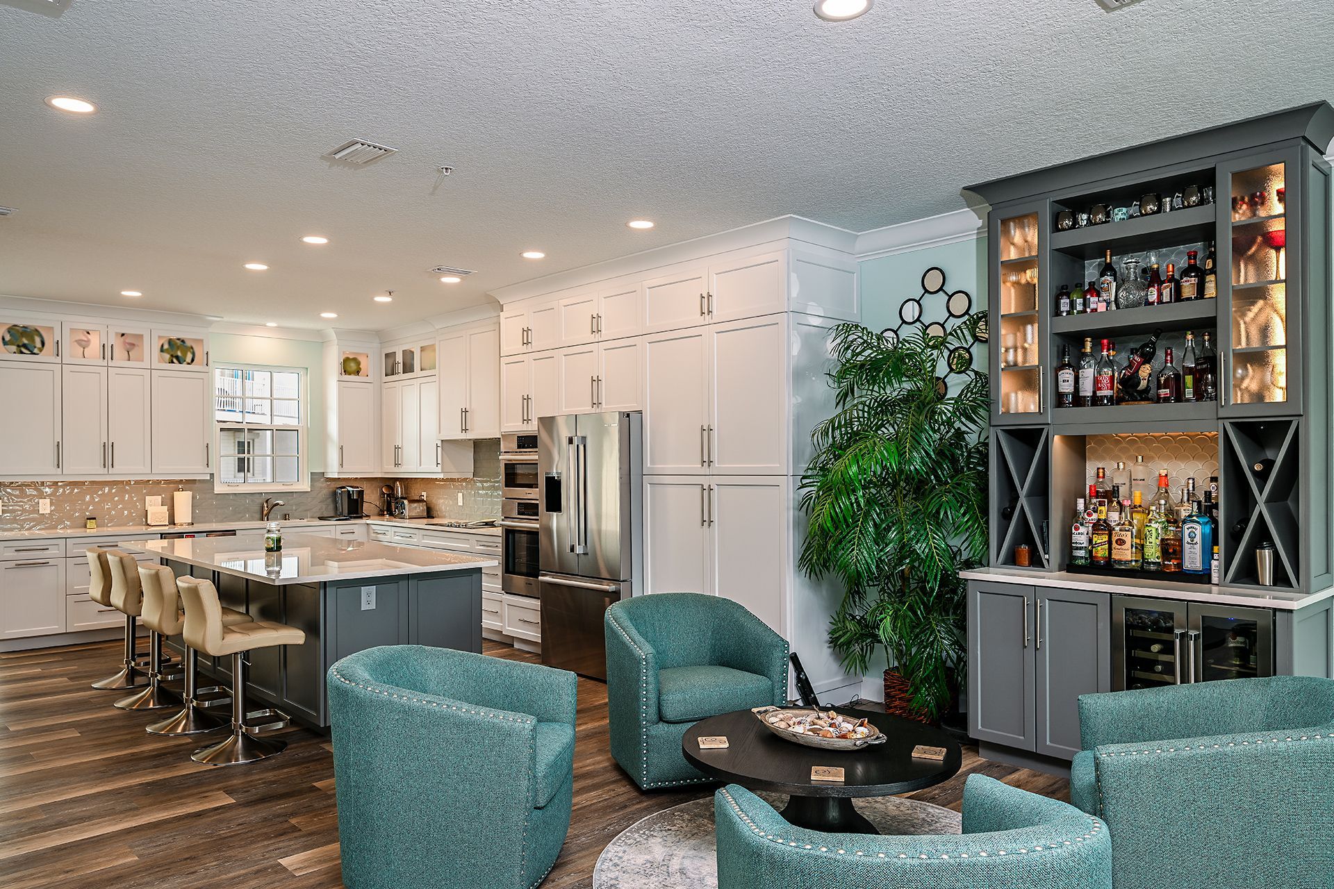 Open-concept kitchen and living room with white cabinets, island seating, teal chairs, and a glass display cabinet