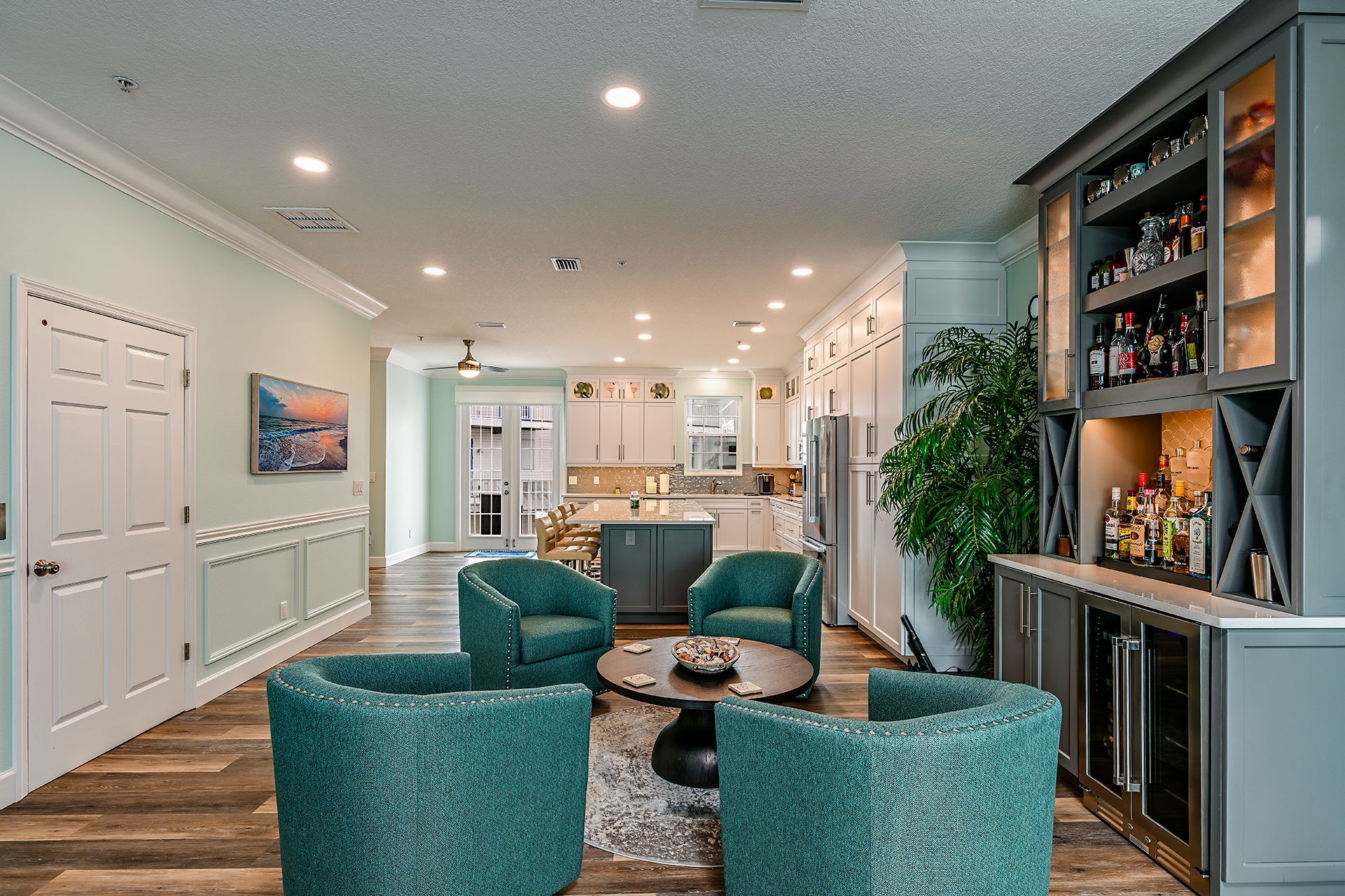 Modern living room with teal chairs, built-in shelving, and a kitchen in the background