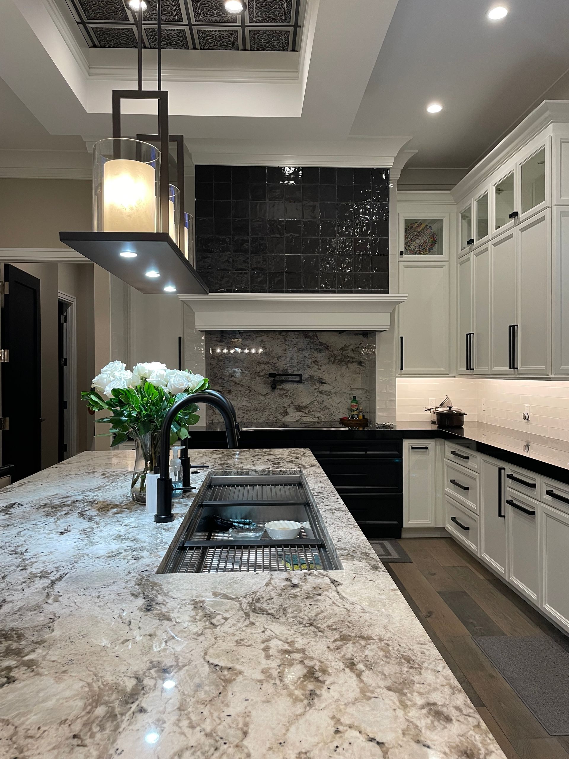 Modern kitchen with a large marble island, black pendant light, white cabinets, and a tiled backsplash.