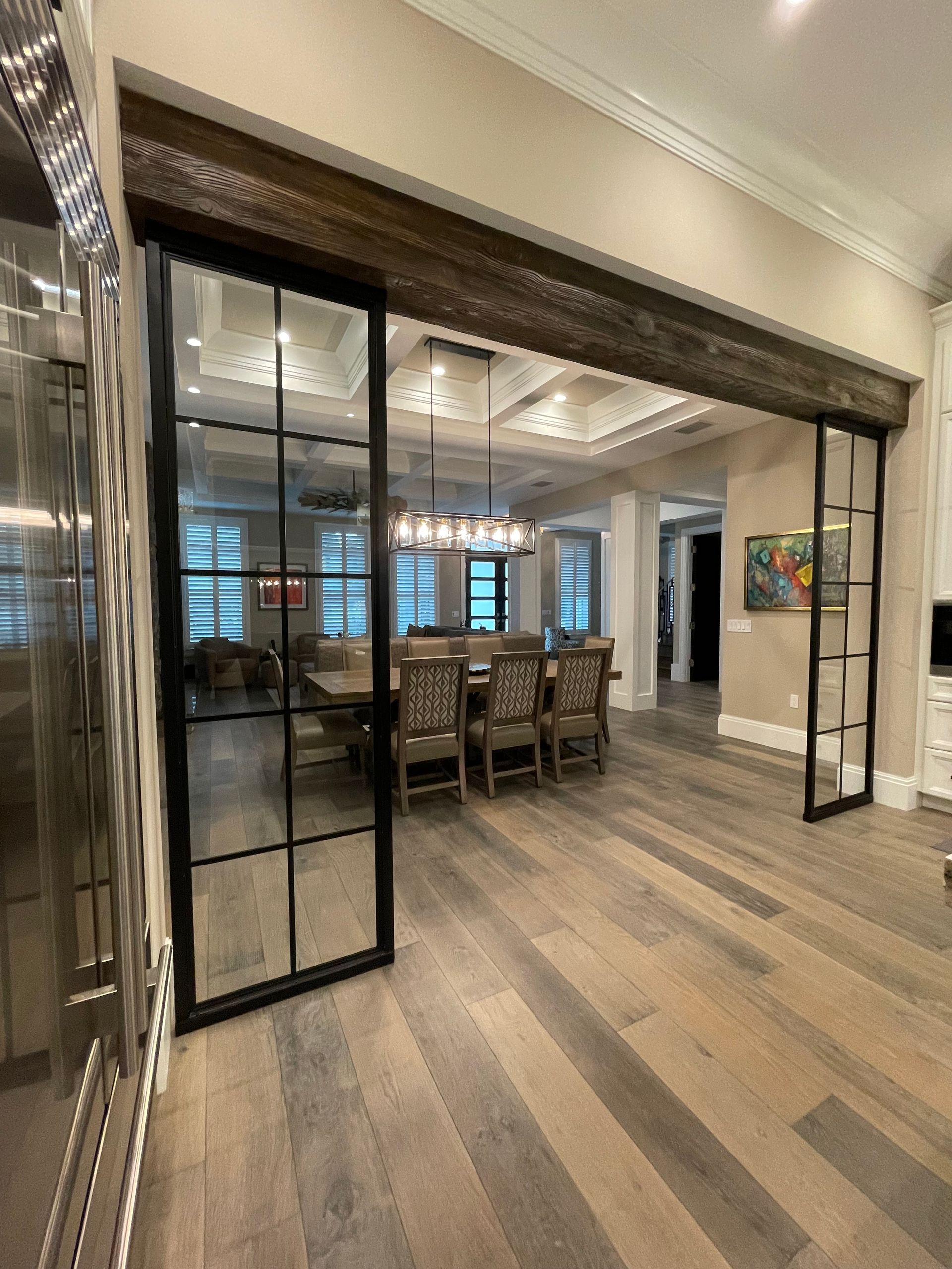 Modern dining room with long wooden table, black-framed glass doors, and wide plank wood floors