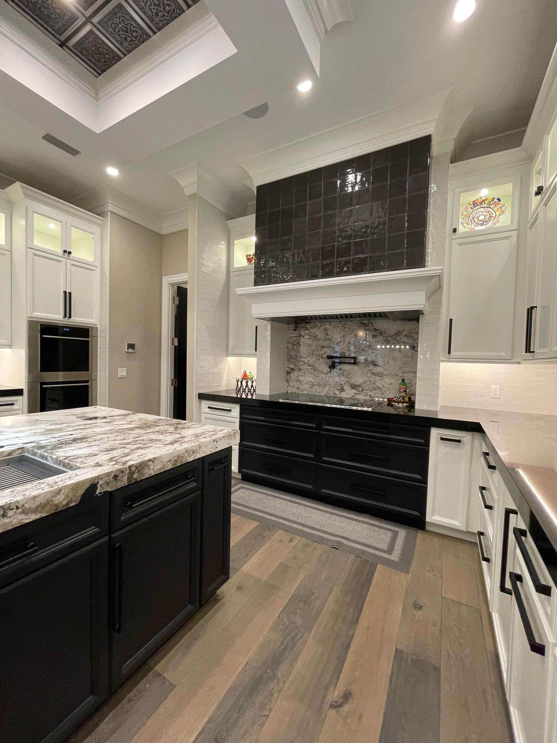 Modern kitchen with dark island, white cabinets, stainless appliances, and large range hood