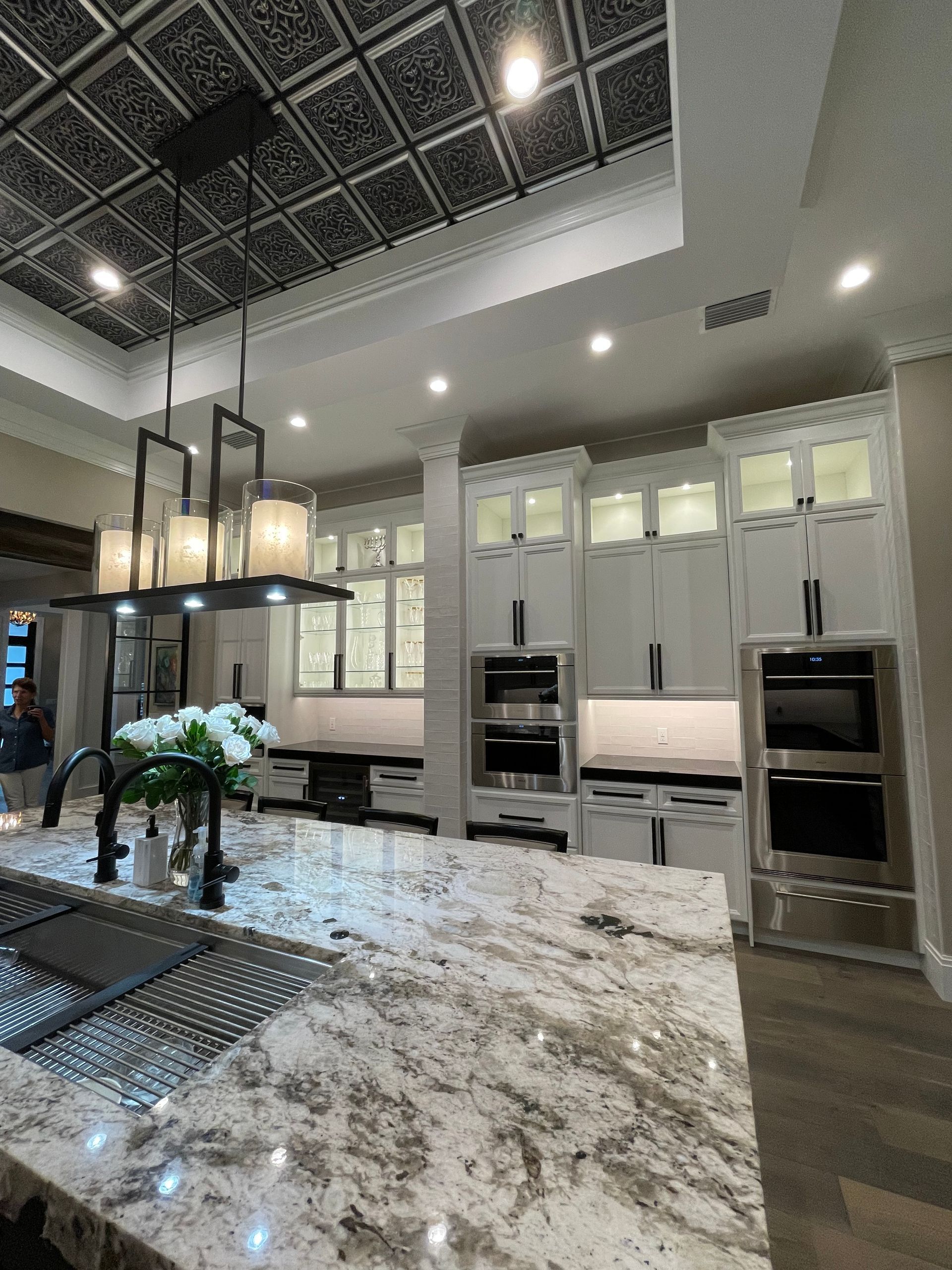 Modern kitchen with white cabinets, large marble island, pendant lights, and built-in ovens