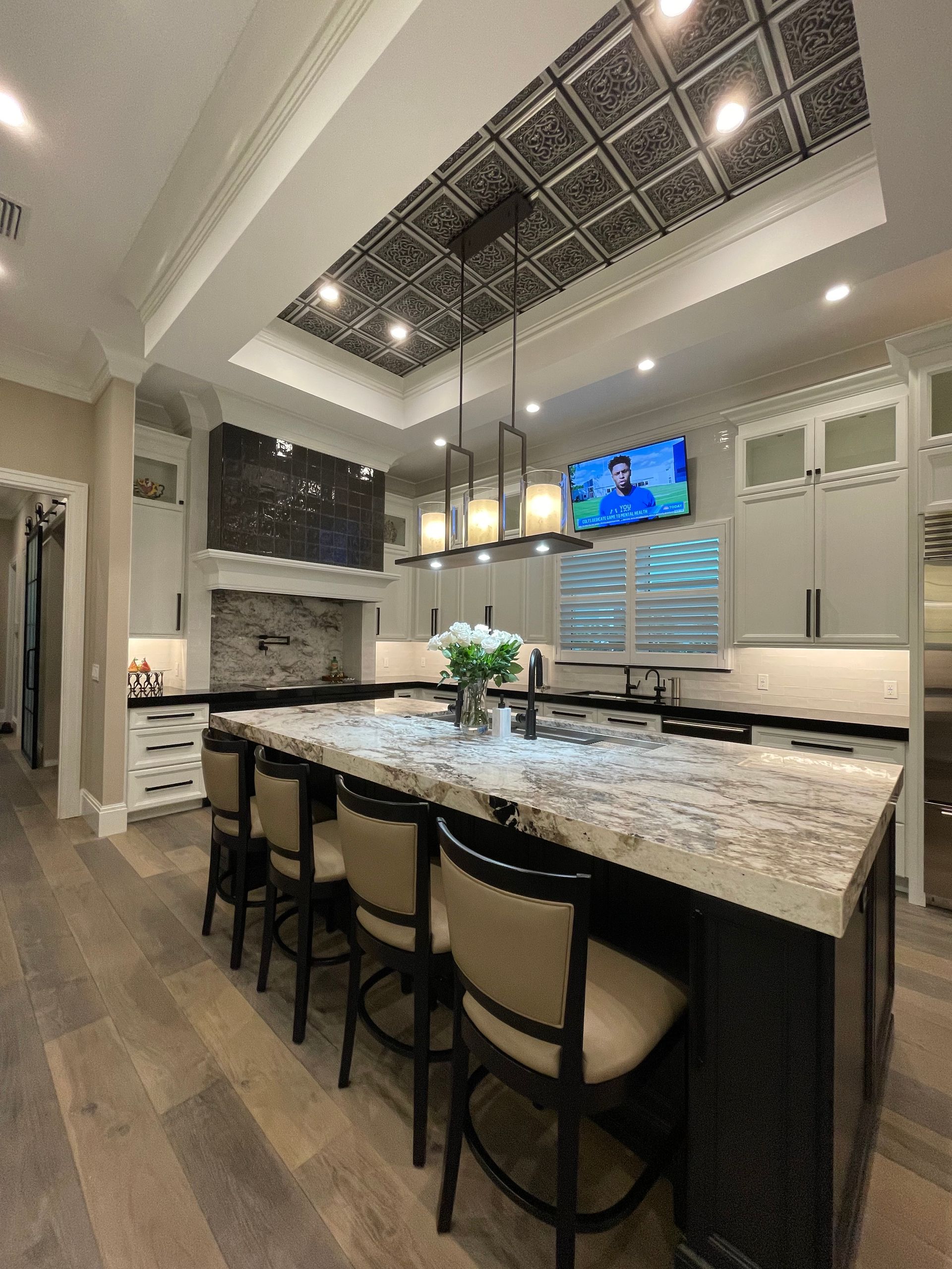 Modern kitchen with a large island, pendant lights, high ceilings, and a TV mounted on the wall.