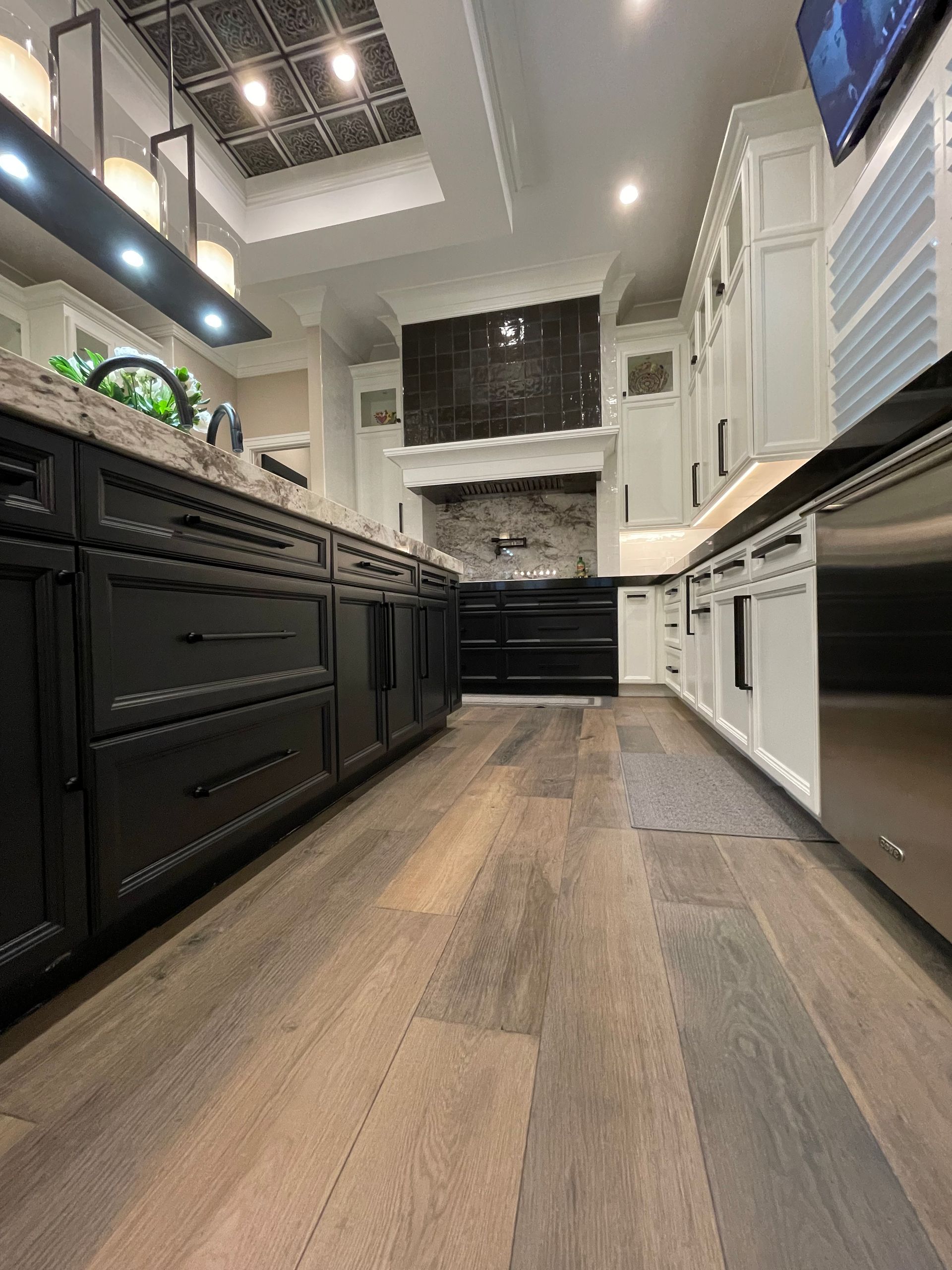 Modern kitchen with black and white cabinets, wood floors, and an island under bright ceiling lights